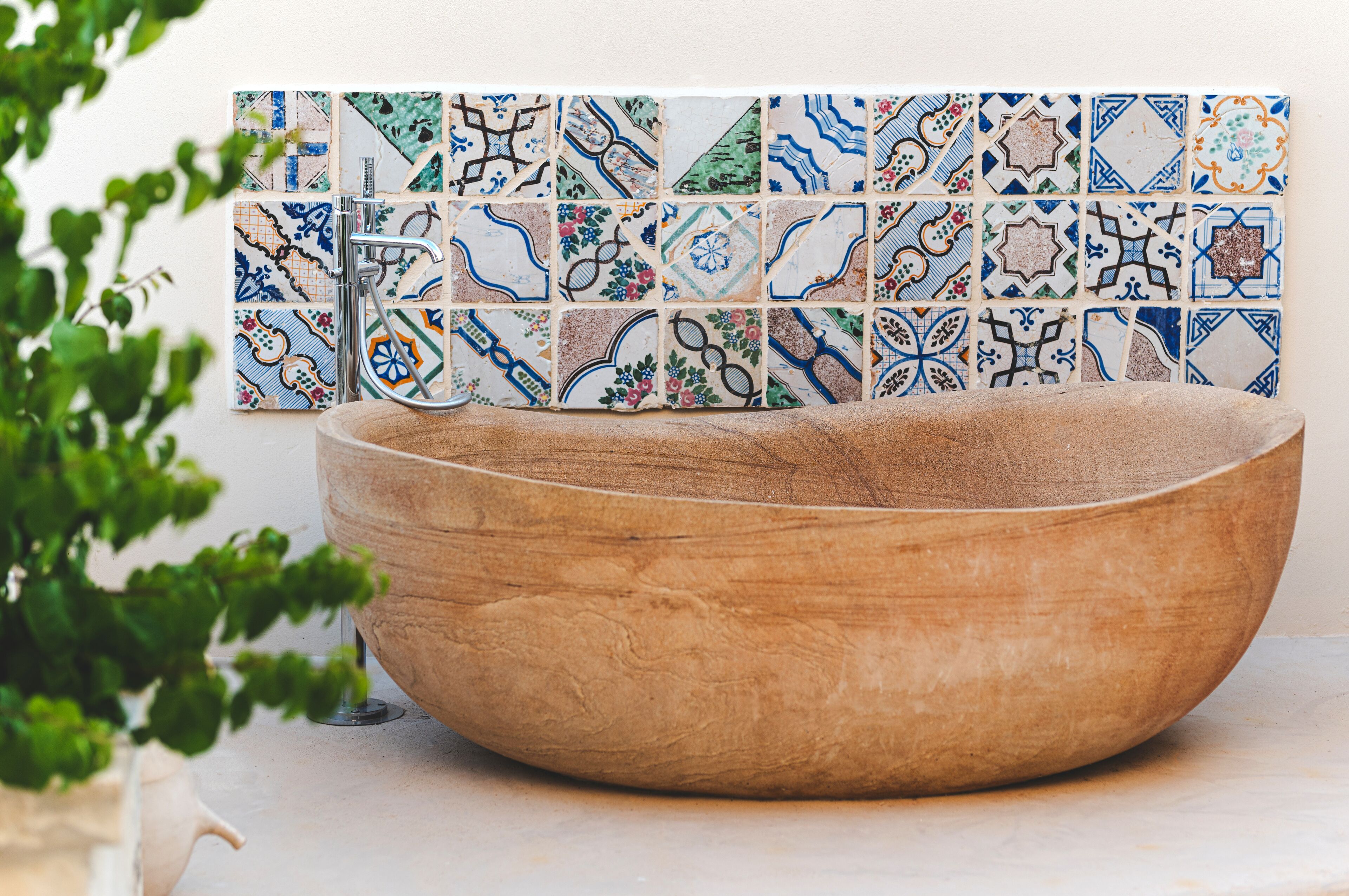 A wooden bowl sink with a modern faucet, set against a tiled backsplash with various patterns.
