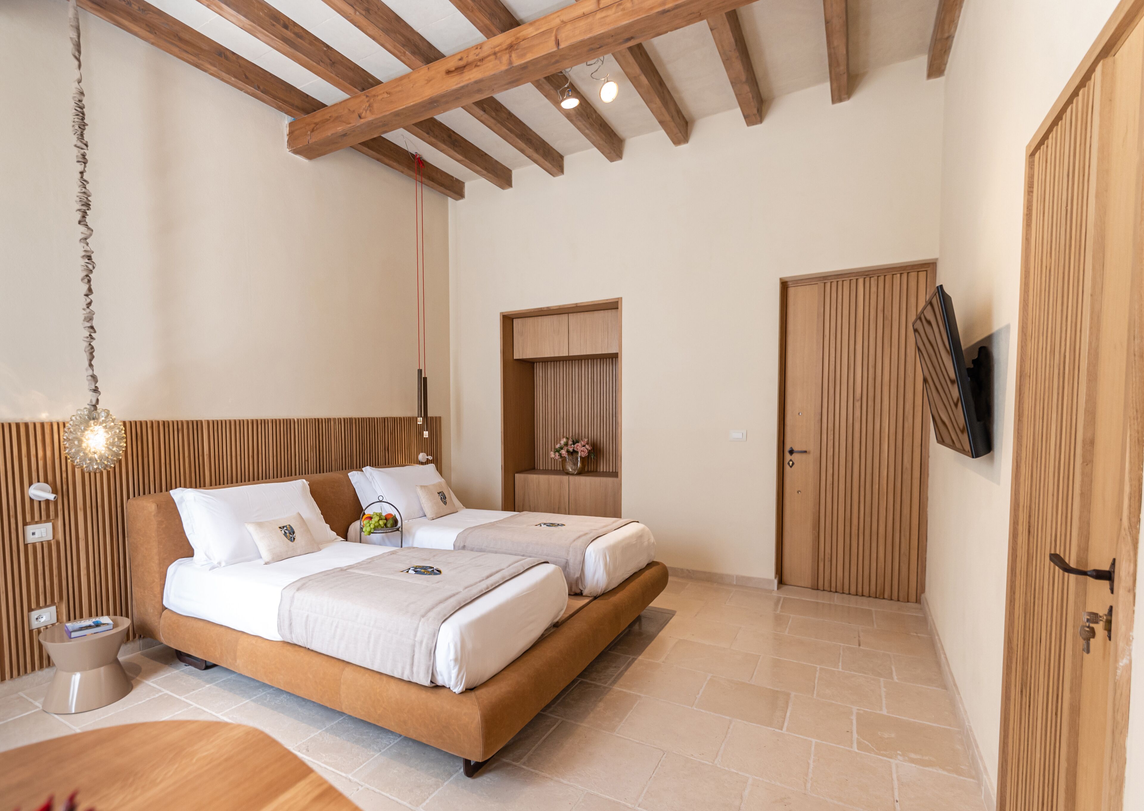 Un dormitorio moderno con techo de madera, una cama con cabecera, una mesita de noche, un televisor montado en la pared y un armario de madera.