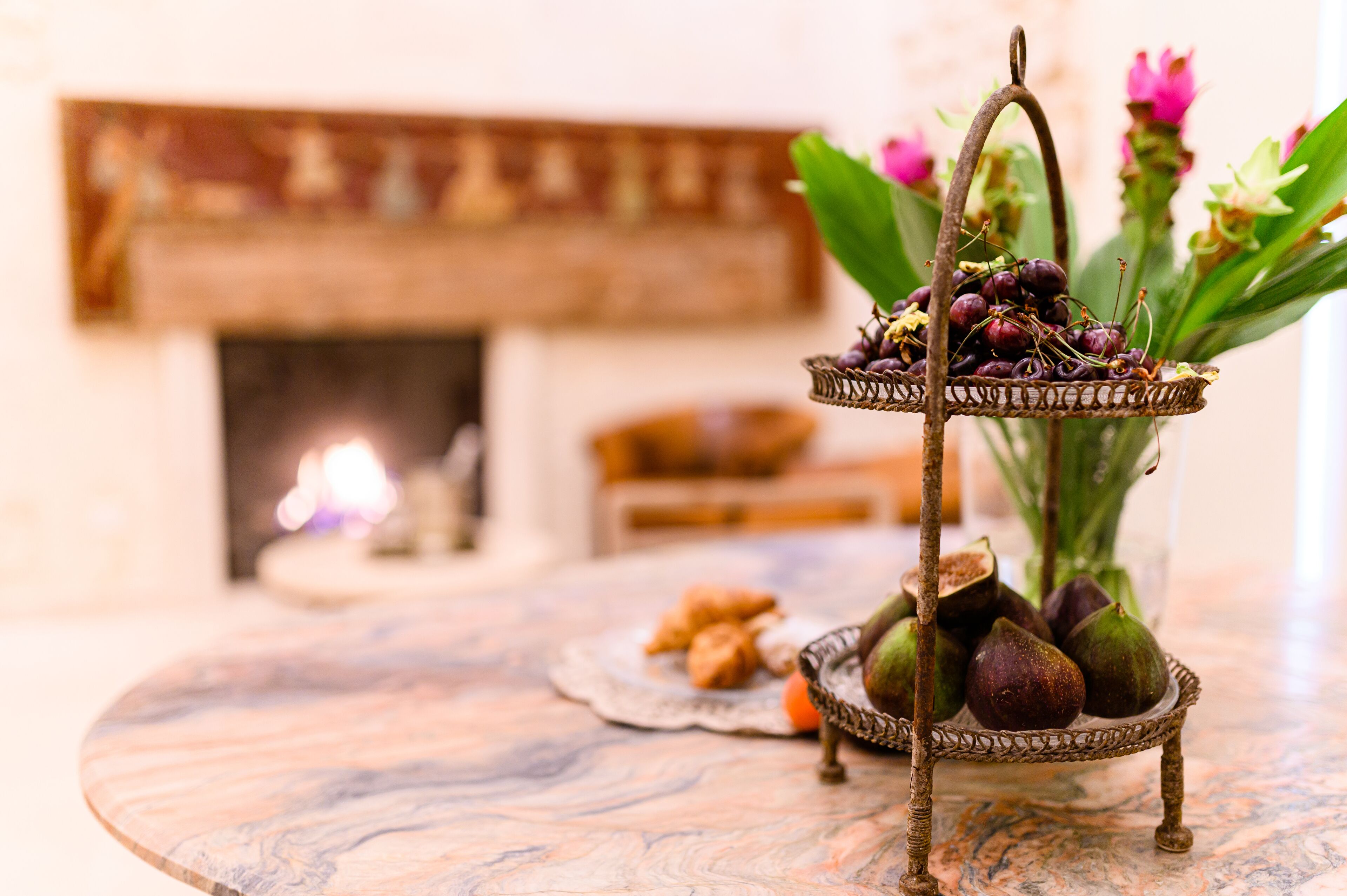 A two-tiered metal stand holding figs and flowers, with a fireplace in the background.