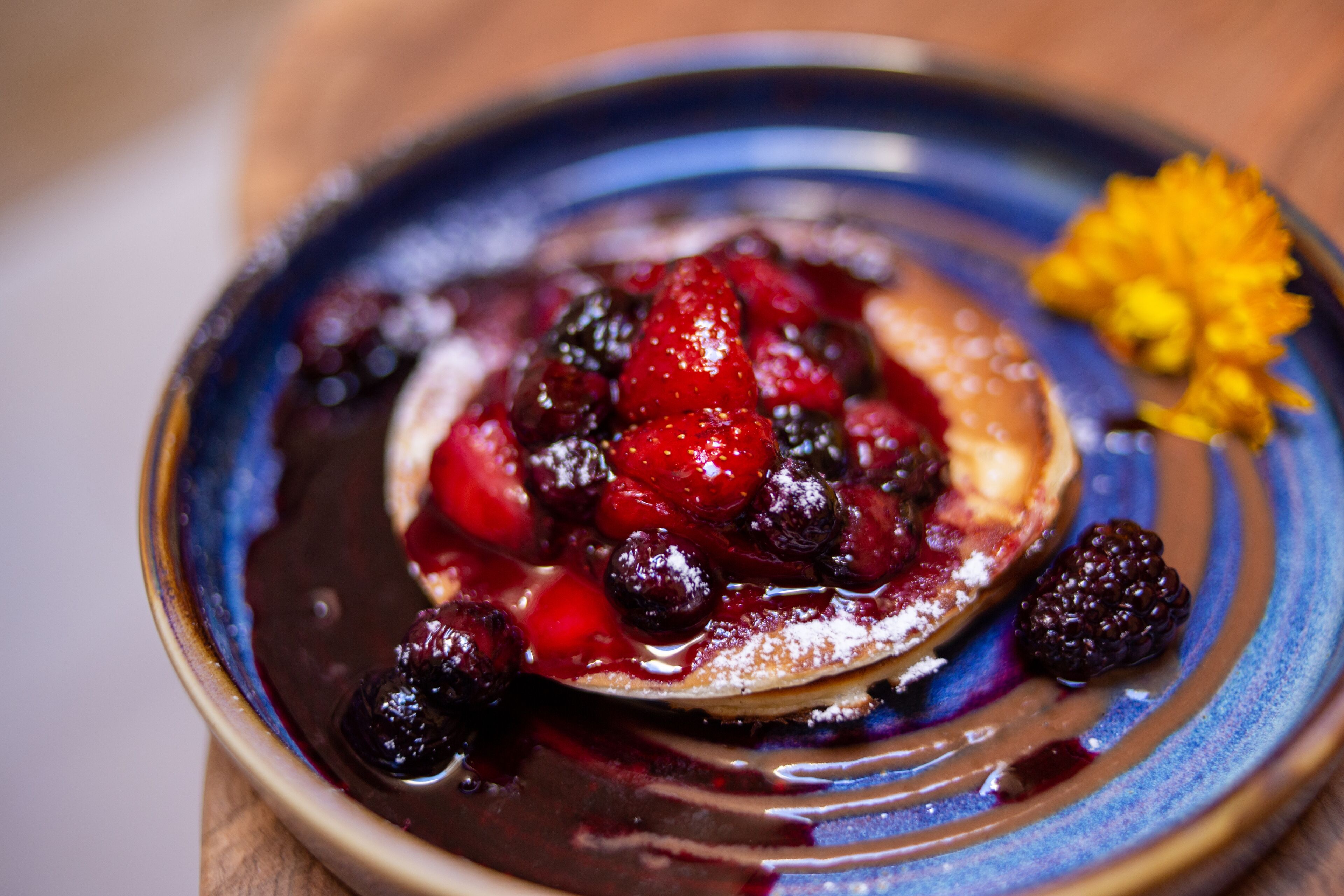 A dessert with berries and a yellow flower on a plate.