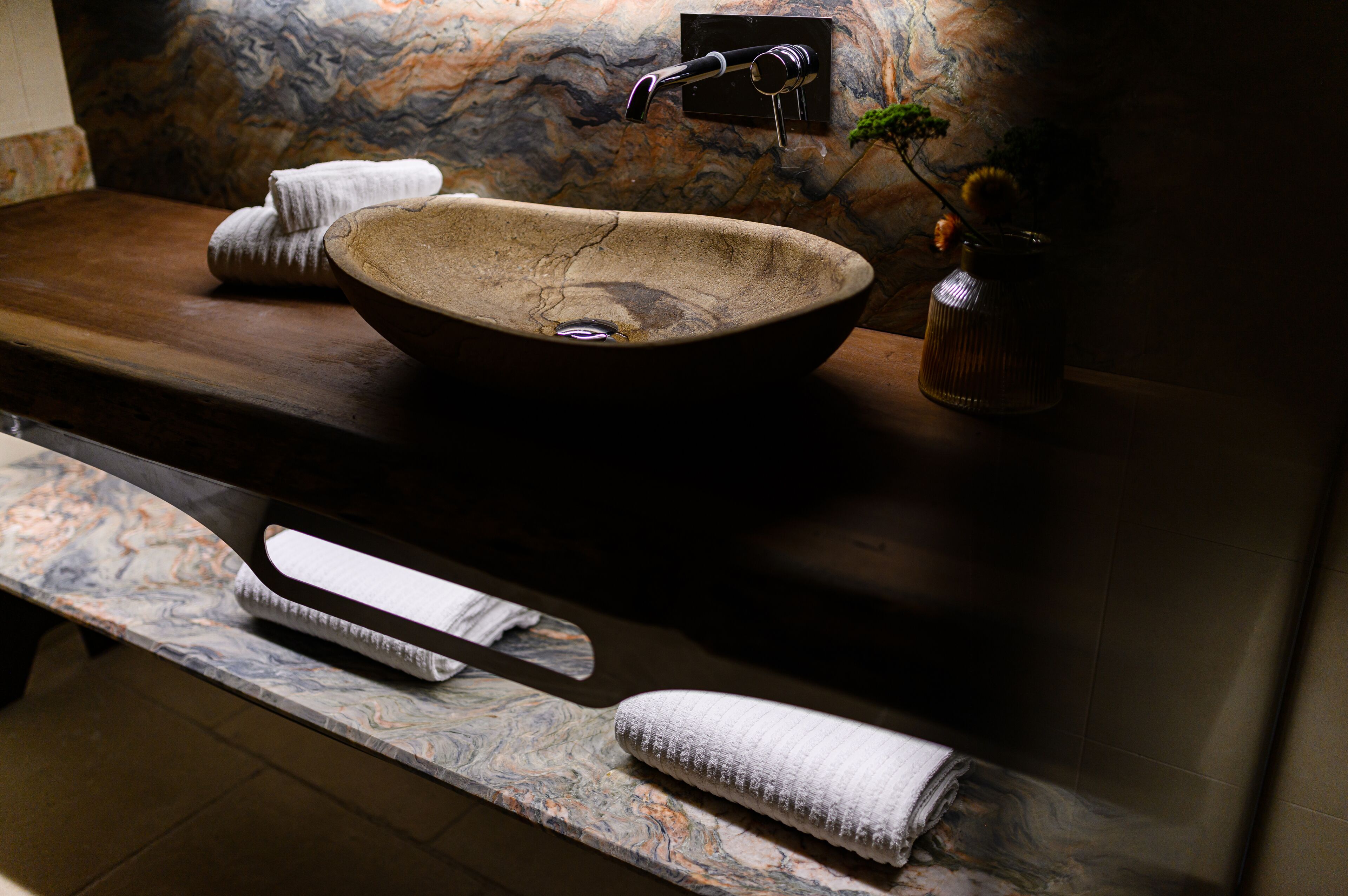A stone sink with a faucet, towels, and a vase with a plant on a marble countertop.
