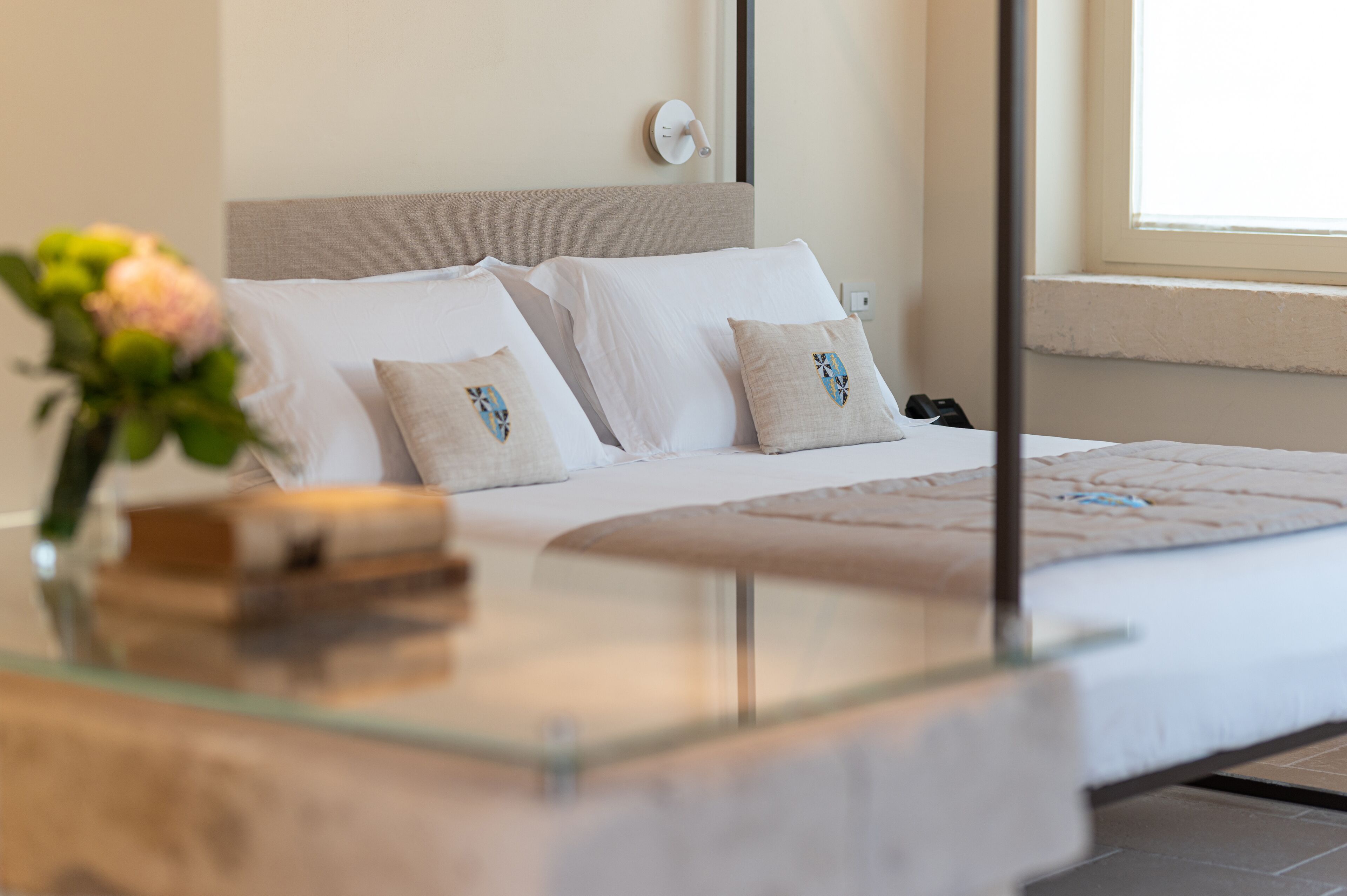 A modern bedroom with a bed, pillows, a bedside table, and a vase with flowers.