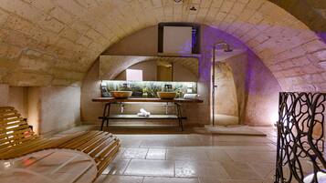A bathroom with a stone arch ceiling, a wooden bench, a sink with a mirror, and a decorative metal partition.