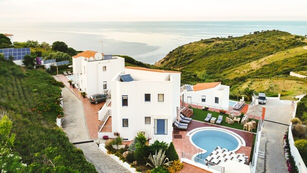 Un bâtiment moderne doté d’une piscine, entouré de verdure et offrant une vue sur la côte.