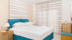 Un lit bien fait, avec du linge de lit blanc, une tête de lit bleue et une table de chevet en bois dotée de tiroirs.