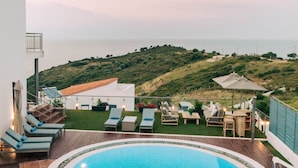 Une piscine à la forme originale, entourée d’une terrasse en bois et de chaises longues.