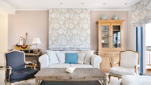 Un salon avec un canapé blanc, des fauteuils bleus et blancs, une table basse en bois et un meuble avec des portes en verre.