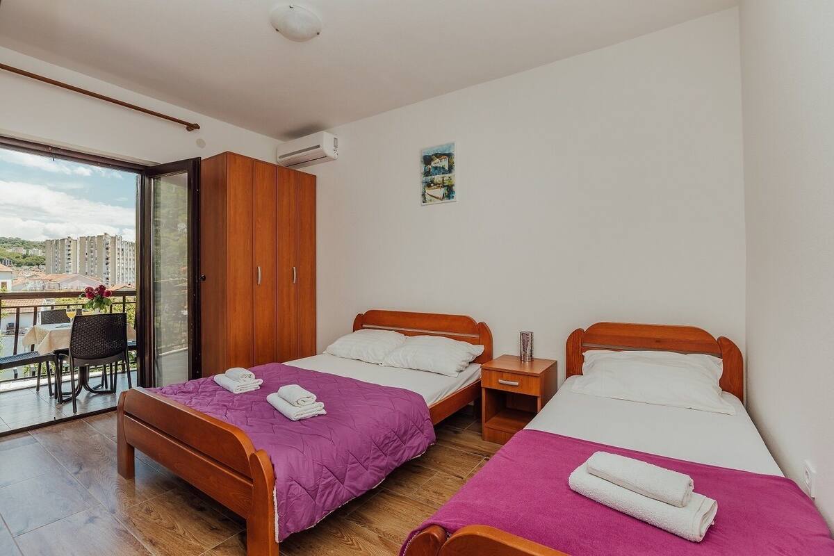 Ein Hotelzimmer mit zwei Holzbett, einem Balkon mit Tisch und Stühlen und Blick auf die Stadt.
