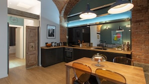 A modern kitchen with a wooden dining table, dark cabinets, and a brick wall. - Casa Bellezia Santa Maria - Design and history in the heart of Turin (Torino)