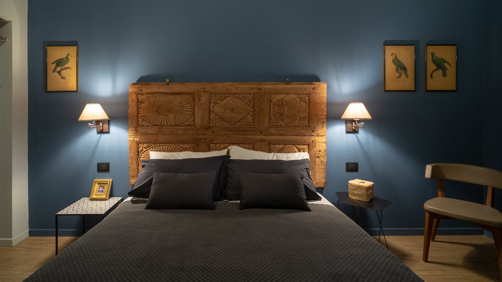 Une chambre à coucher avec un grand lit, deux lampes de chevet, une tête de lit en bois et des œuvres d’art encadrées accrochées aux murs.