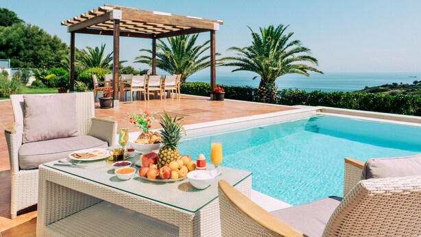 A poolside area with a table set for breakfast, a pergola, and a view of the sea. - Aries Villas | Villa Sagittarius – Private Pool & Aegean Sea Views (Skiathos)