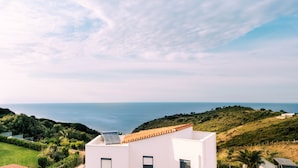 A coastal view with a modern building featuring a solar panel, surrounded by greenery and overlooking the sea. - Aries Villas | Villa Sagittarius – Private Pool & Aegean Sea Views (Skiathos)