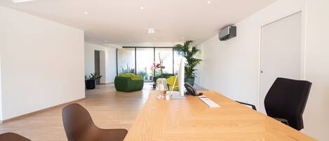A modern meeting room with a wooden table, two chairs, a computer, and a potted plant.