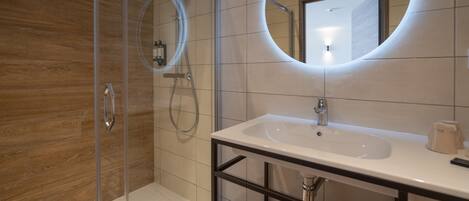A modern bathroom with a glass shower enclosure, a white sink with a black frame, and a large mirror with a circular light.