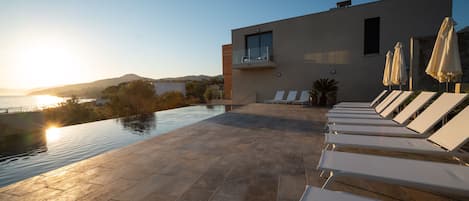 Ein Poolbereich im modernen Stil mit Liegestühlen und Sonnenschirmen, mit Blick auf ein Gewässer und eine Berglandschaft.