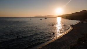A beach with boats, a clear sky, and a sun setting or rising. - Residence Saletta Mare (L'Île-Rousse)