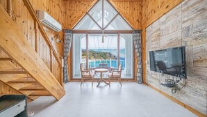 Interior de una cabaña de madera con comedor, un televisor en una pared de piedra y una escalera.
