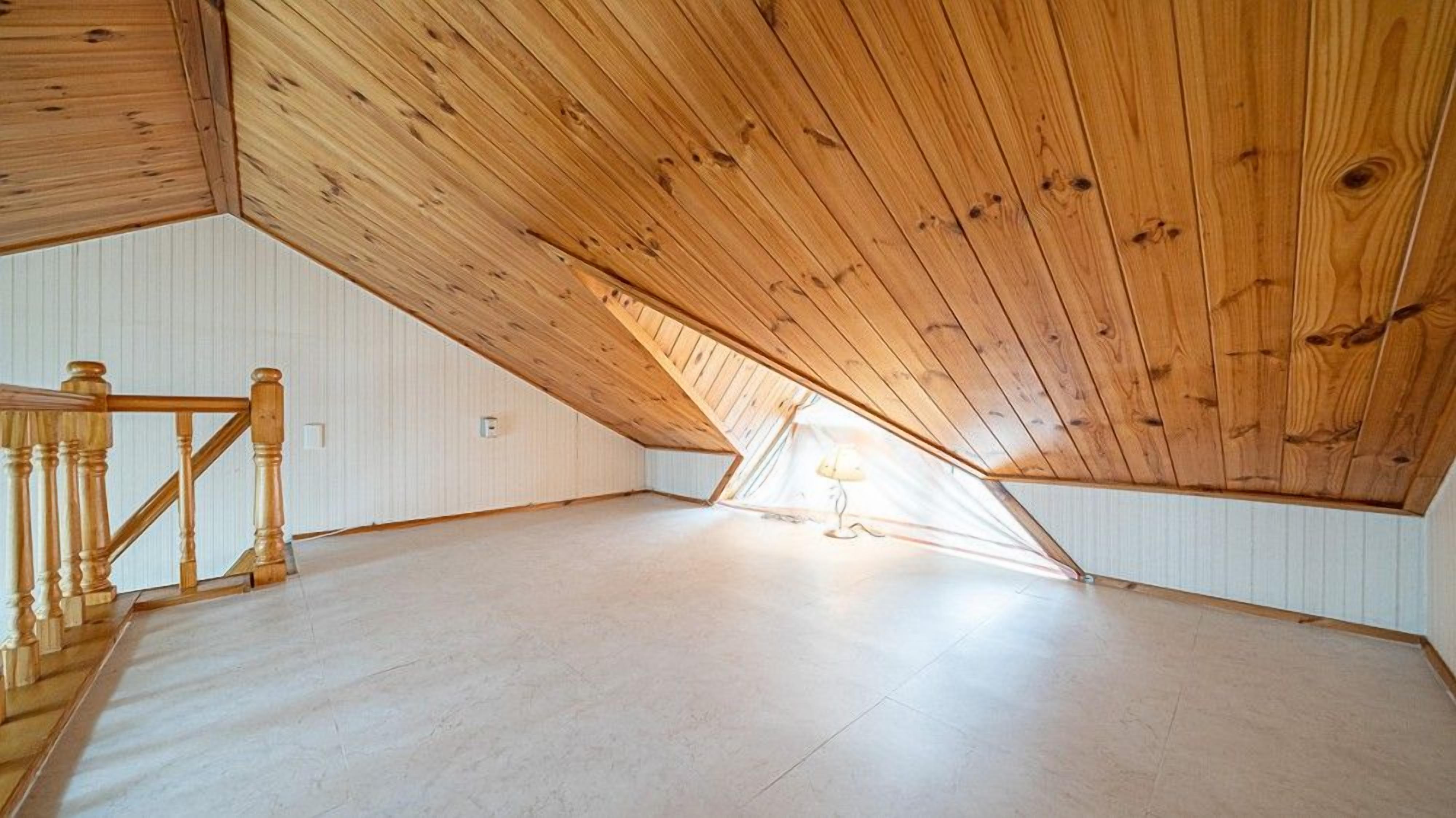 A spacious attic room with wooden beams and a sloped ceiling.