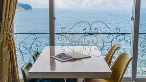 Una mesa con dos copas de vino y un libro abierto, frente a una vista panorámica del océano desde un balcón con barandillas de metal decorativo.