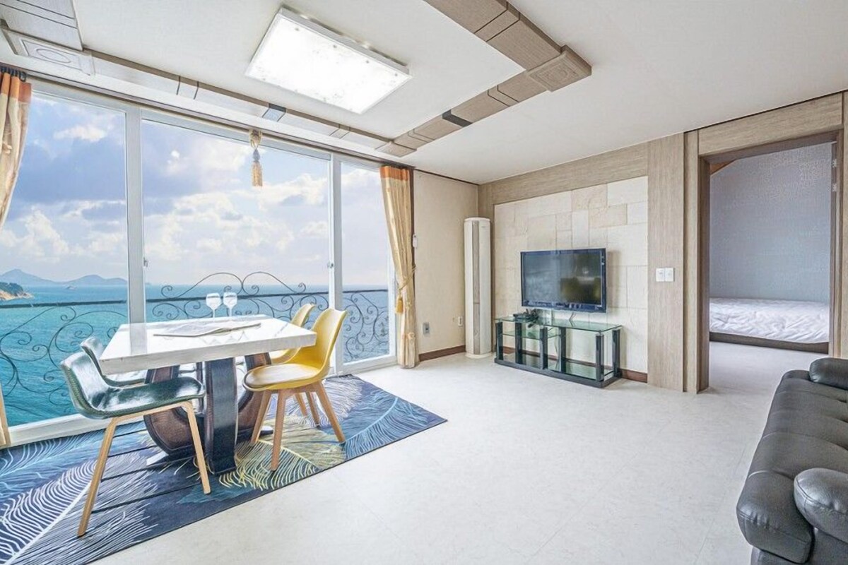 A modern hotel room with a balcony, a dining area, a TV, and a sofa.