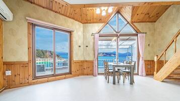 A room with a large window, a dining table with chairs, and a wooden staircase.