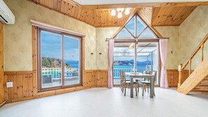A room with a large window, a dining table with chairs, and a wooden staircase. - White O Pension (Geoje)