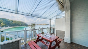 A covered balcony with a table and benches, overlooking a coastal area with clear blue waters and a distant shoreline. - White O Pension (Geoje)