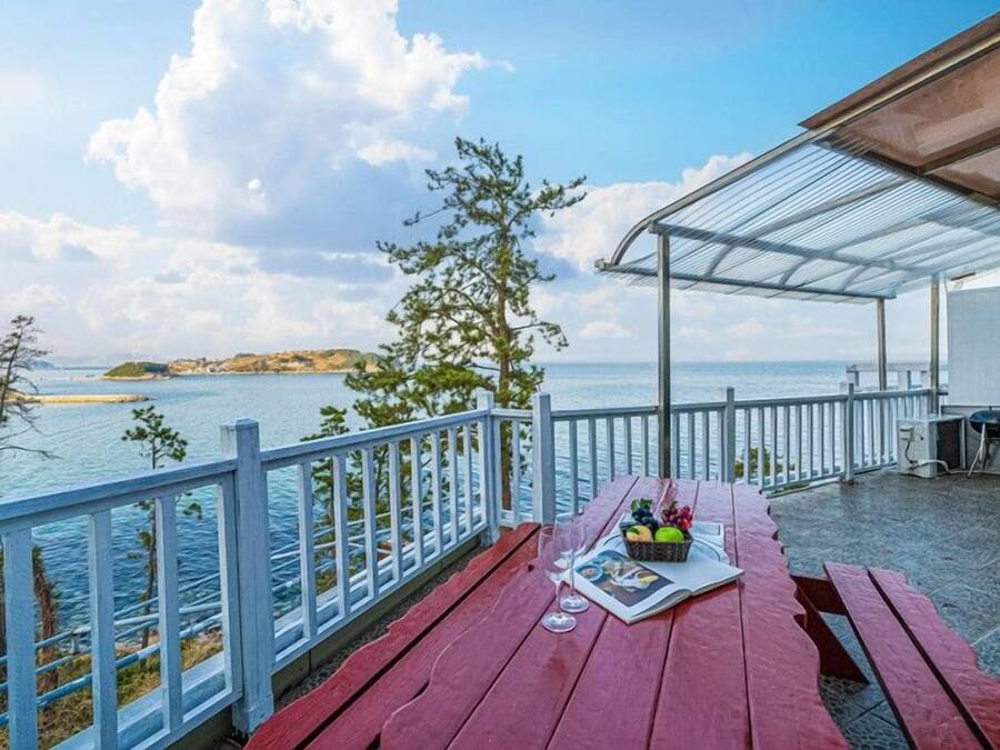 A wooden deck with a picnic table, a grill, and a view of the sea and a distant island.