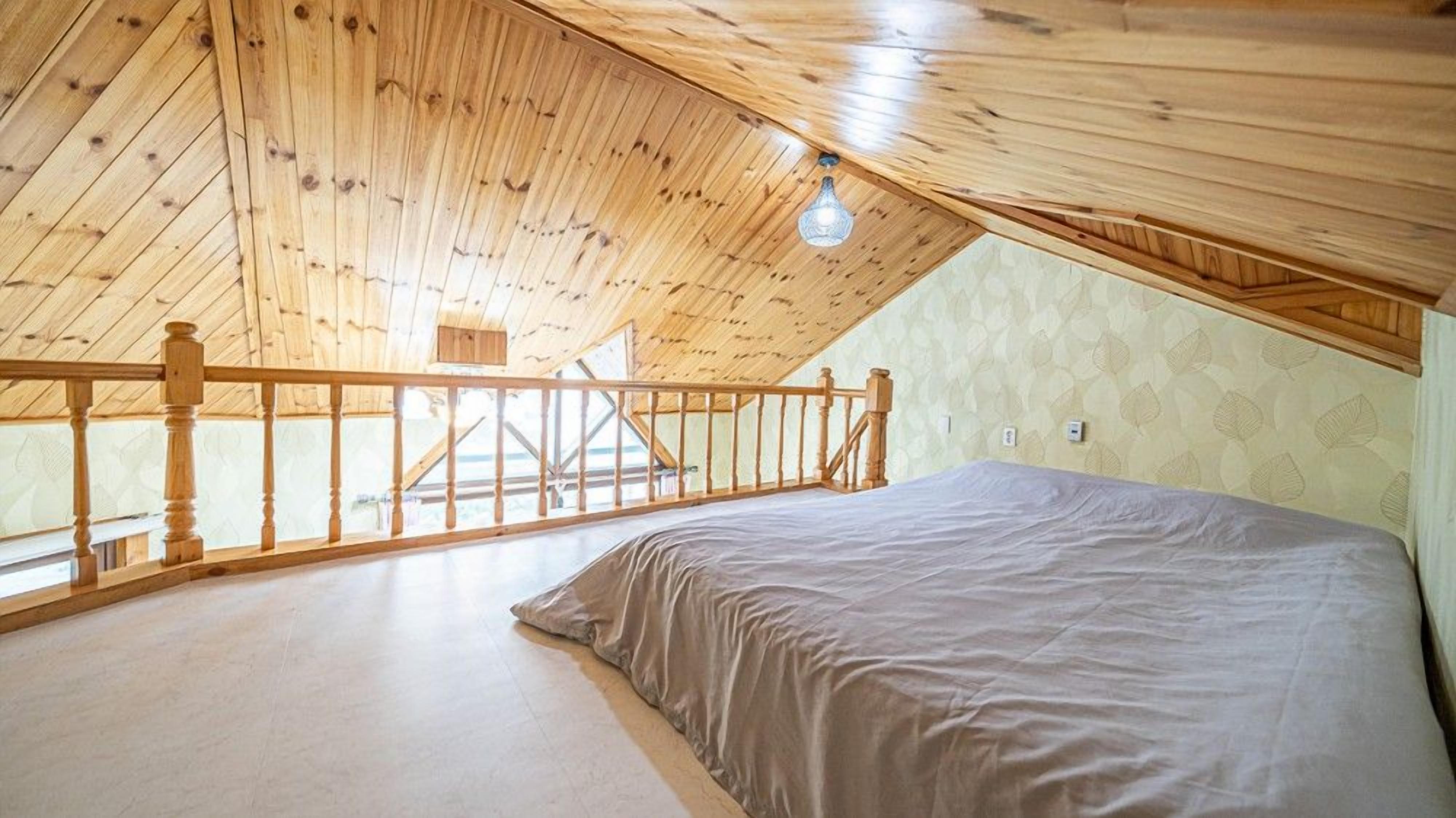 A bedroom with a sloped ceiling, wooden railing, and a bed.