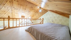 A bedroom with a sloped ceiling, wooden railing, and a bed. - White O Pension (Geoje)