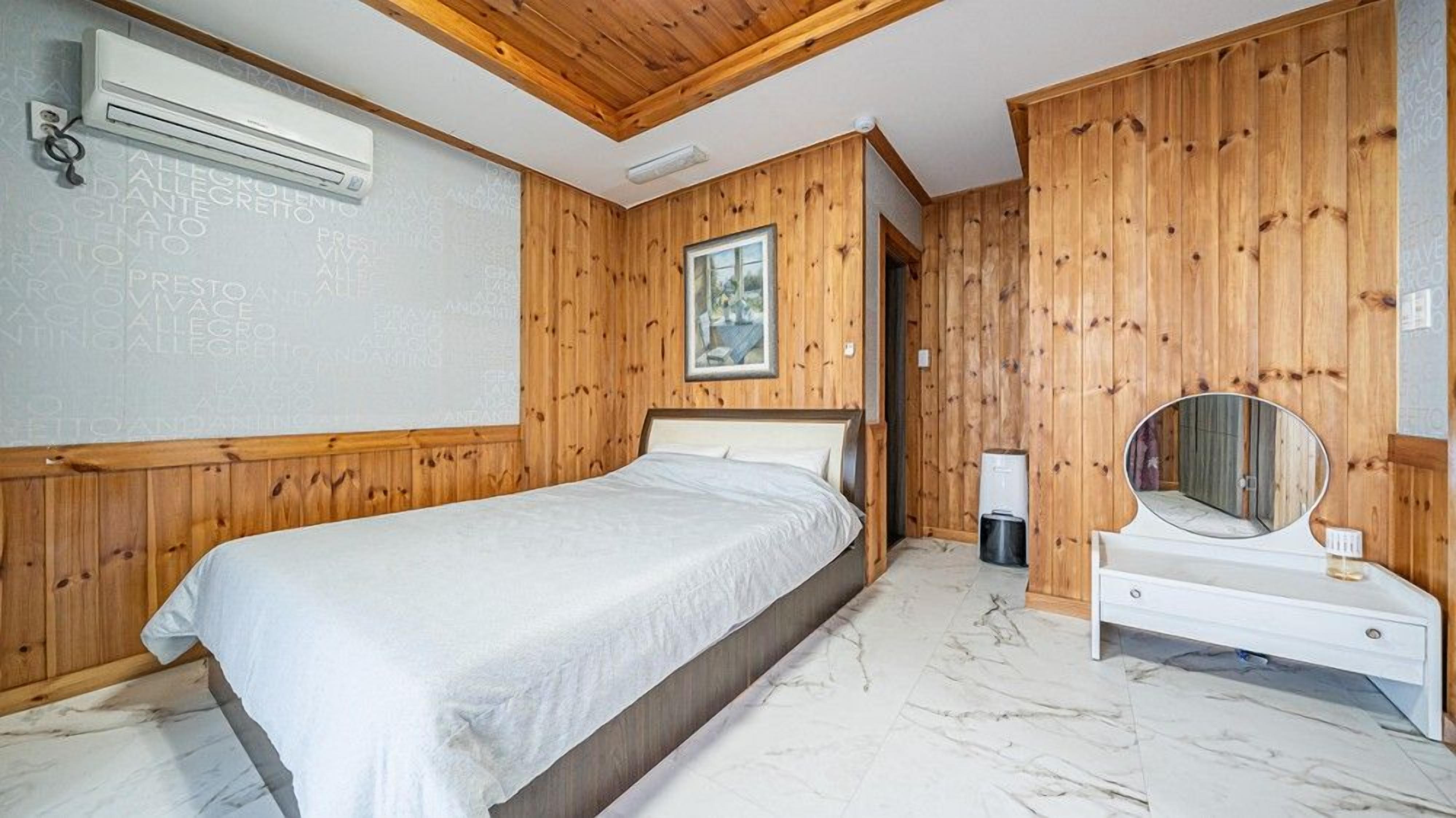 Une chambre à coucher avec un lit, une table de chevet dotée d’un miroir et des lambris en bois sur les murs.