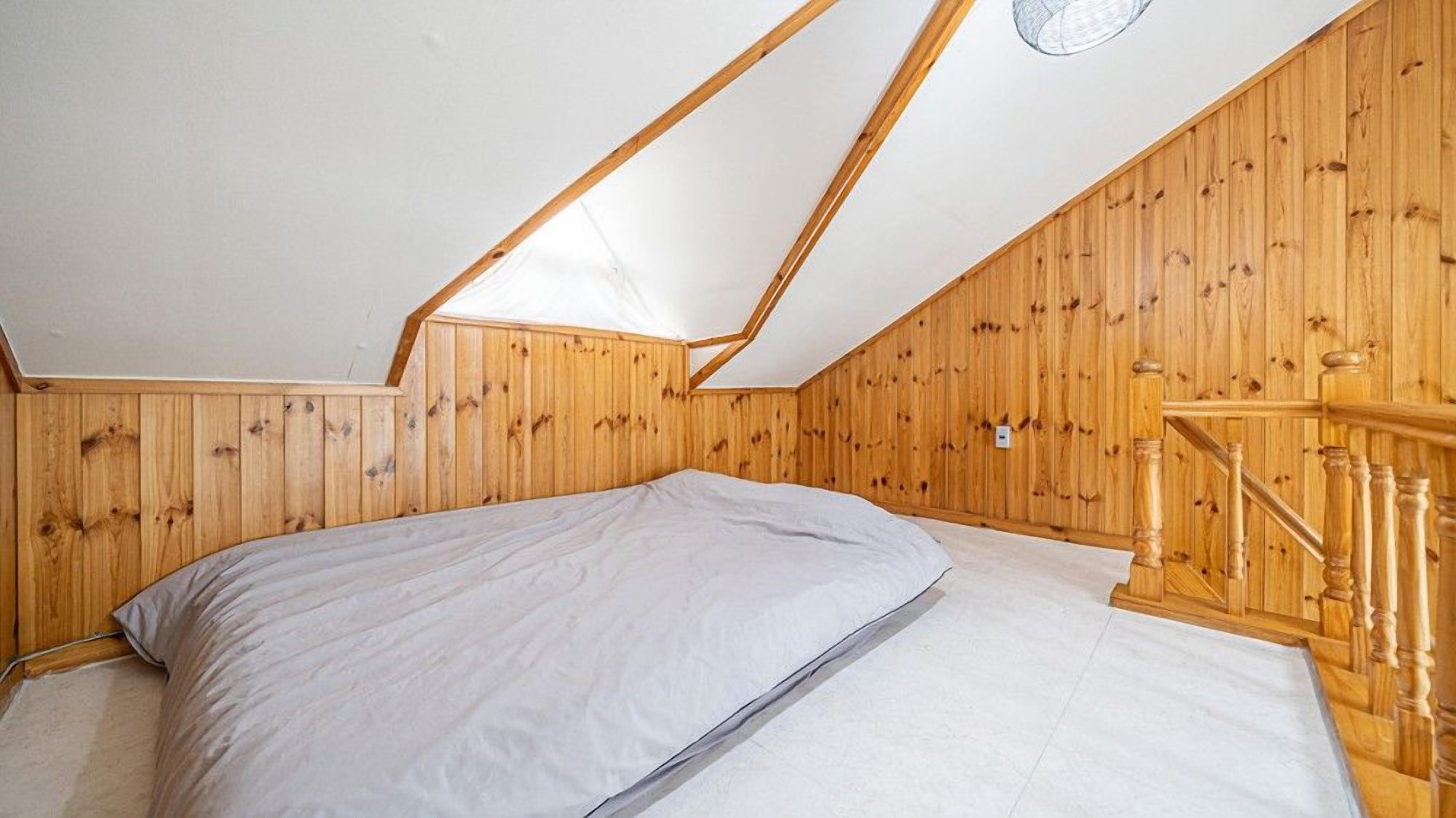 A bedroom with a sloped ceiling, wooden walls, a bed, and a wooden staircase.
