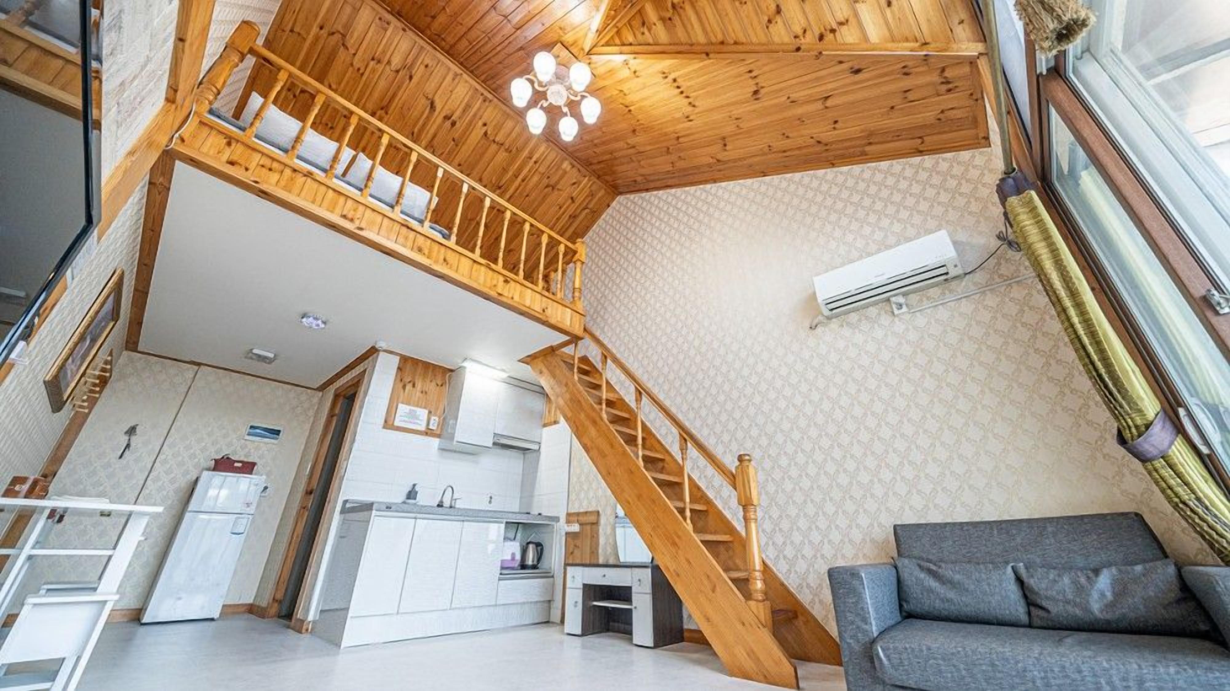 Ein Loft-Zimmer mit einer Holztreppe, einer Küchenzeile und einem grauen Sofa.