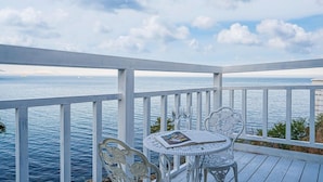 Um deck externo branco com mesa e cadeiras com vista para o mar.