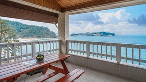 A wooden deck with a picnic table and a view of the sea and a distant island. - White O Pension (Geoje)