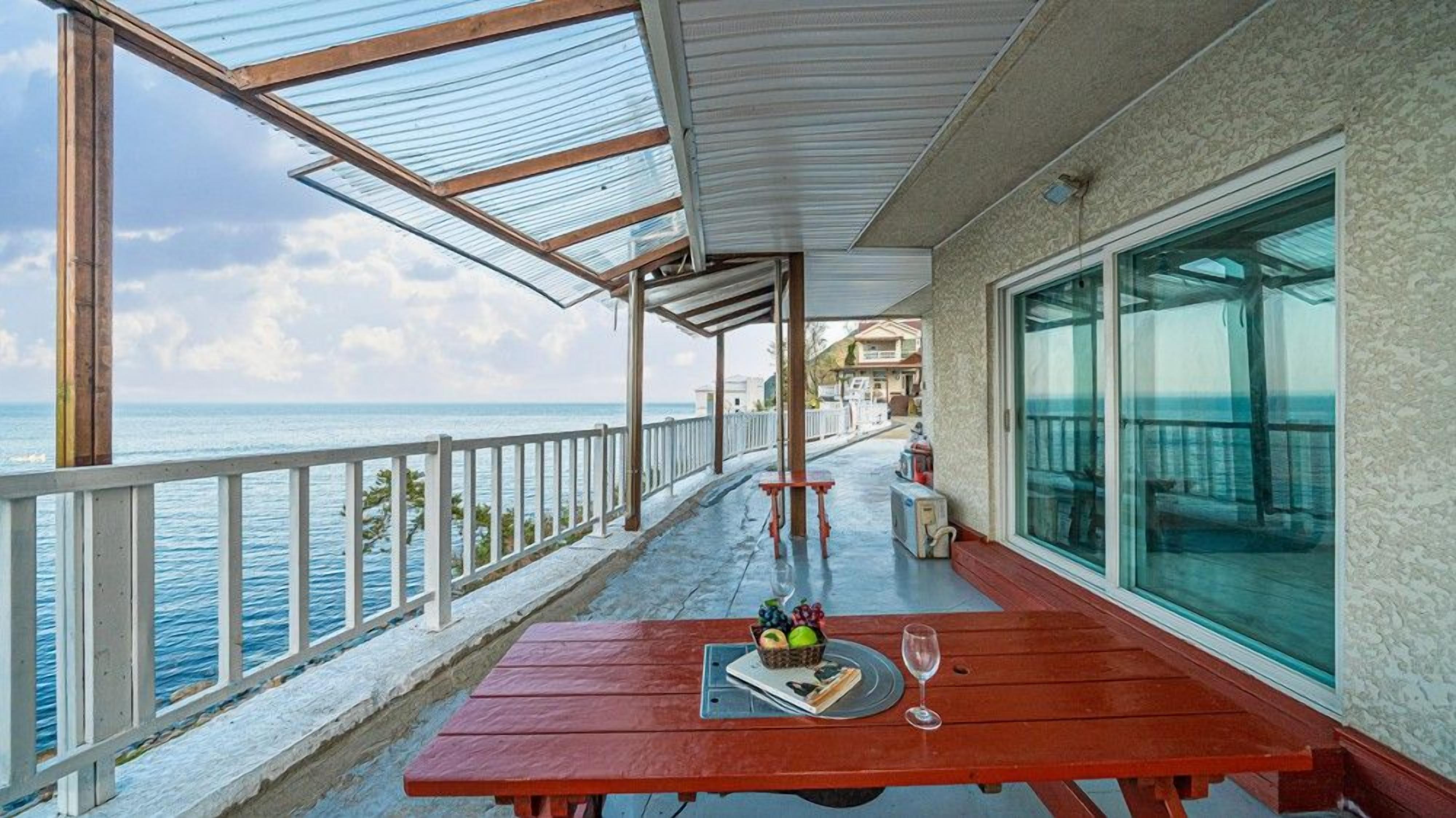 Un espacio al aire libre cubierto con una mesa de madera, barandilla de vidrio y vista al mar.