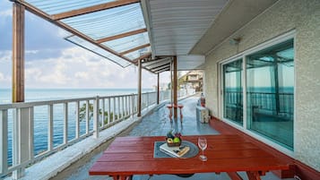 Un espacio al aire libre cubierto con una mesa de madera, barandilla de vidrio y vista al mar.