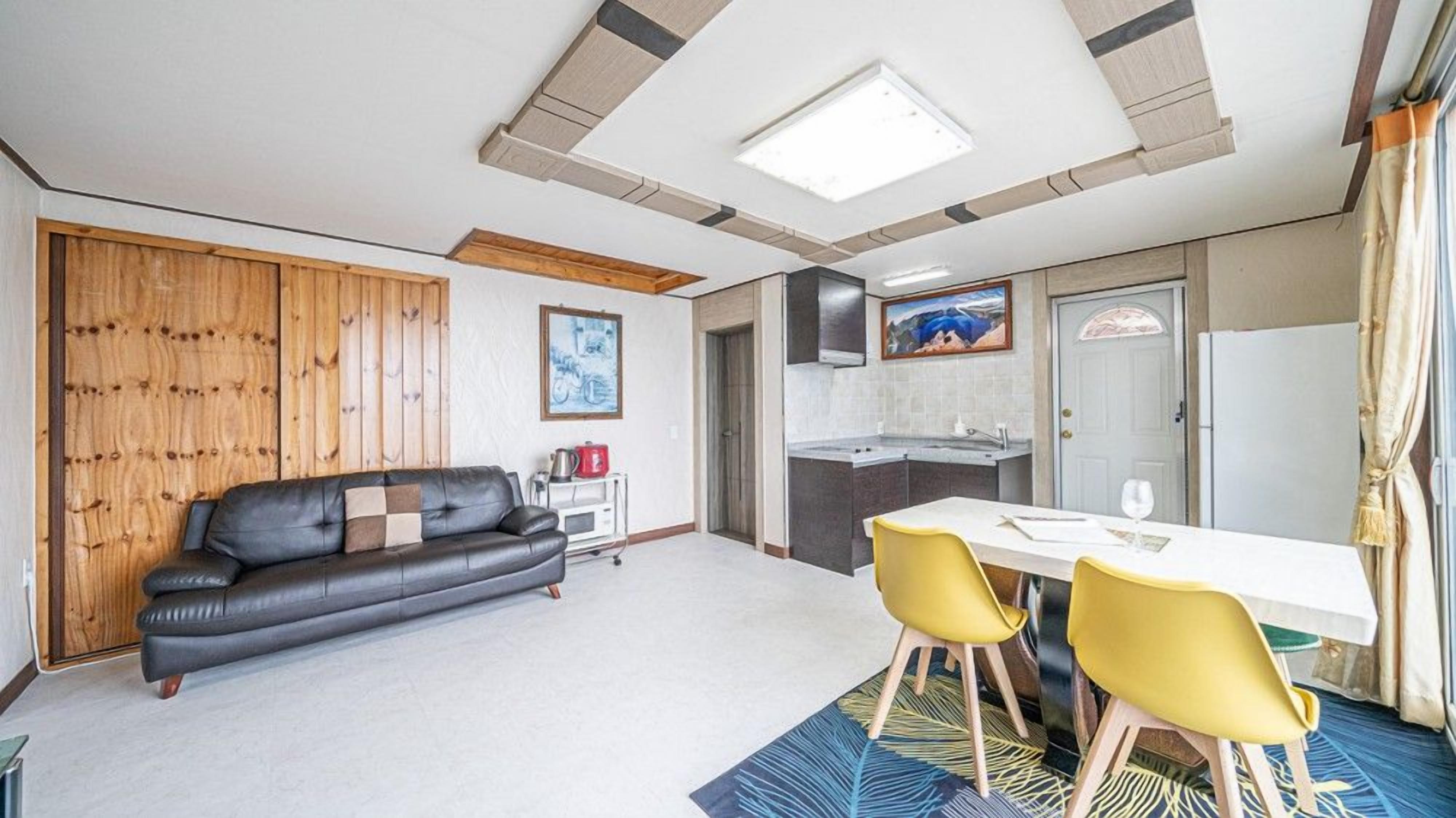 A compact living space with a sofa, dining table, chairs, kitchenette, and a ceiling with skylights.