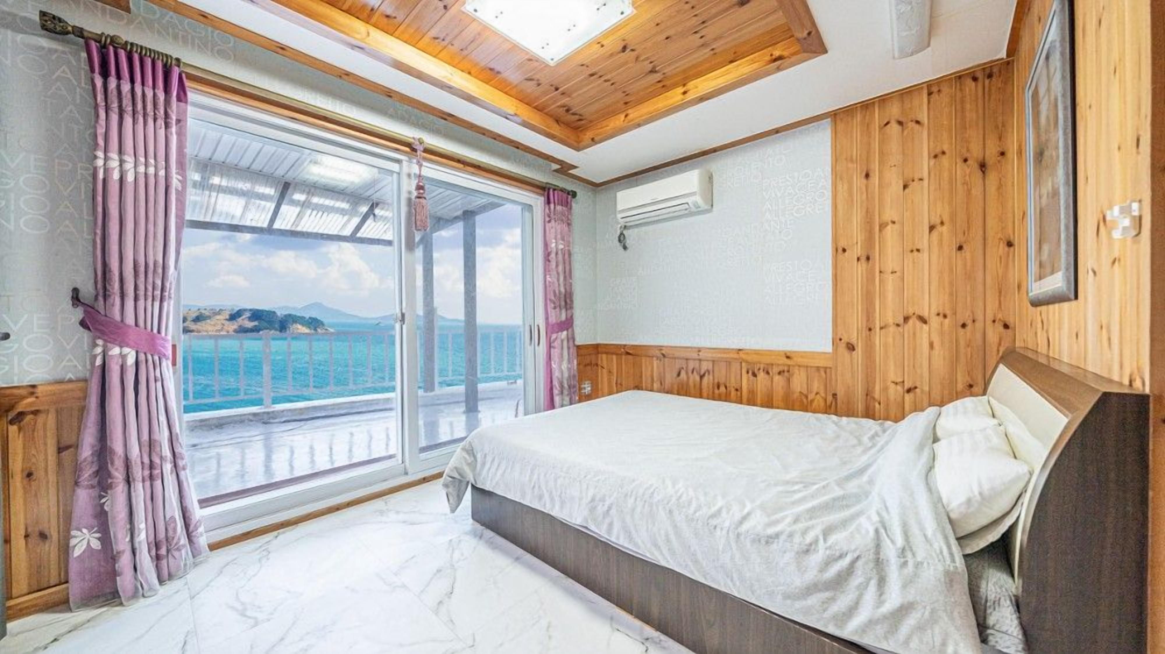 A bedroom with a bed, wooden paneling, a window with curtains, and an air conditioning unit.