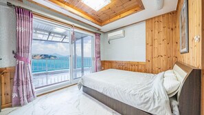A bedroom with a bed, wooden paneling, a window with curtains, and an air conditioning unit.