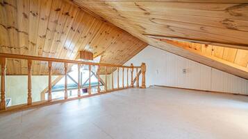An attic room with wooden beams, a wooden staircase, and a skylight.
