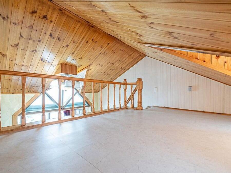 An attic room with wooden beams, a wooden staircase, and a skylight.