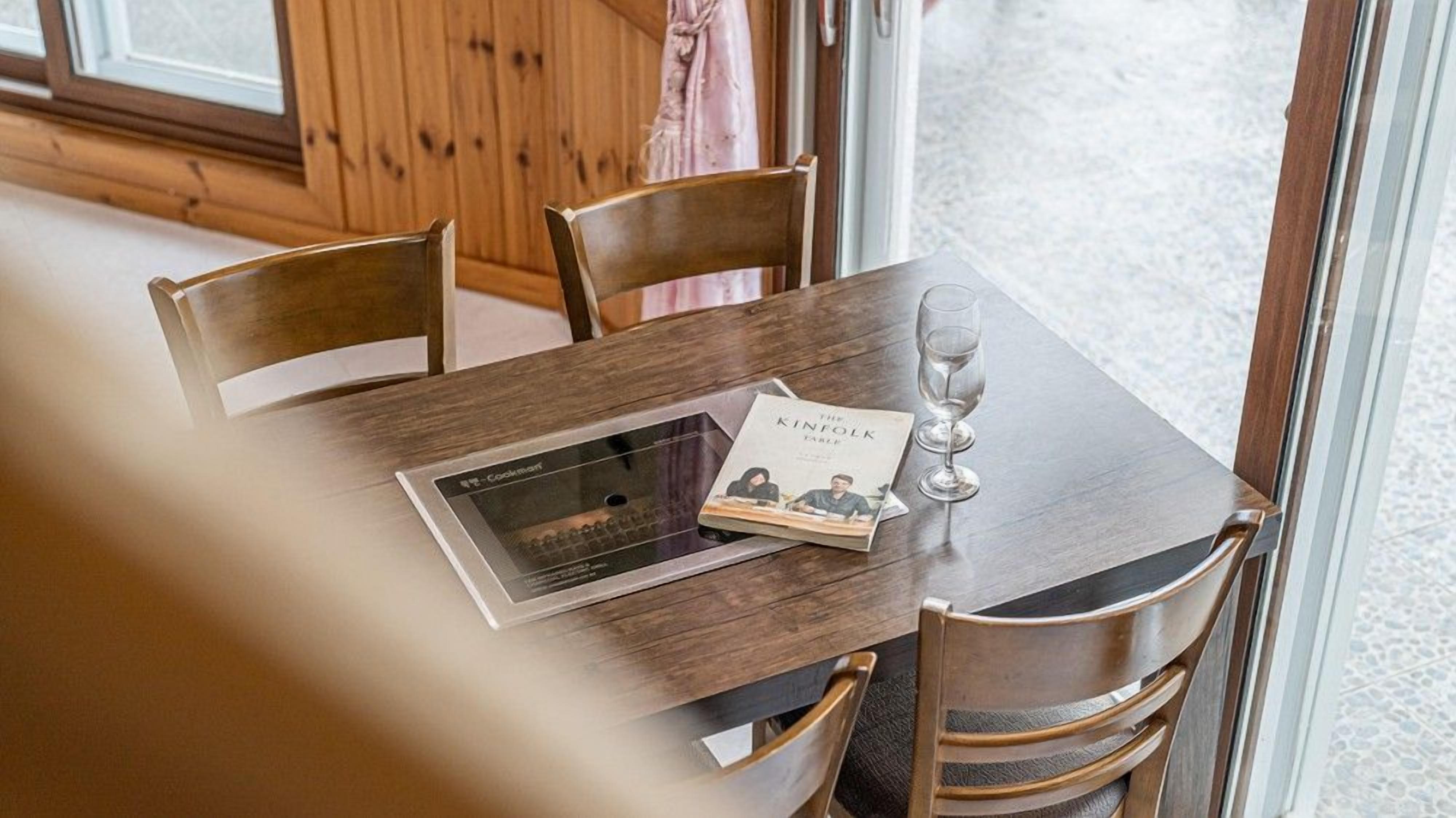 A wooden dining table with a tablet, a book titled "The Kinfolk Table," and a wine glass.