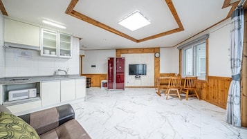Cocina compacta con armarios blancos, microondas y refrigerador rojo. Hay un comedor con sillas de madera y una mesa, y un televisor montado en la pared.