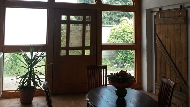 Ein Essbereich mit Holztisch und -stühlen, einem Blumentopf und einem großen Bogenfenster mit Blick auf Grünfläche.