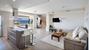 A modern living room with a kitchen area, a sofa, a coffee table, and a TV mounted on the wall. - AMAZING DUPLEX NEXT TO THE BEACH IN MARBELLA (Marbella)