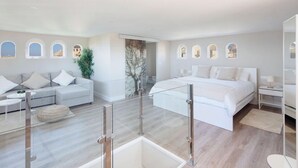 A modern bedroom with a large bed, a sofa, and a glass partition. - AMAZING DUPLEX NEXT TO THE BEACH IN MARBELLA (Marbella)