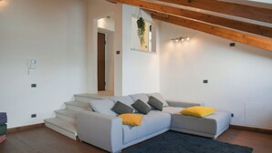 Ein modernes Wohnzimmer mit grauem Ecksofa, Holzbalken, einer Treppe und einer hängenden Pflanze.