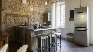 A kitchen with a stone wall, wooden beams, a stainless steel refrigerator, and a bar area with stools. - CA’ DEL BUSO   (VERONA)