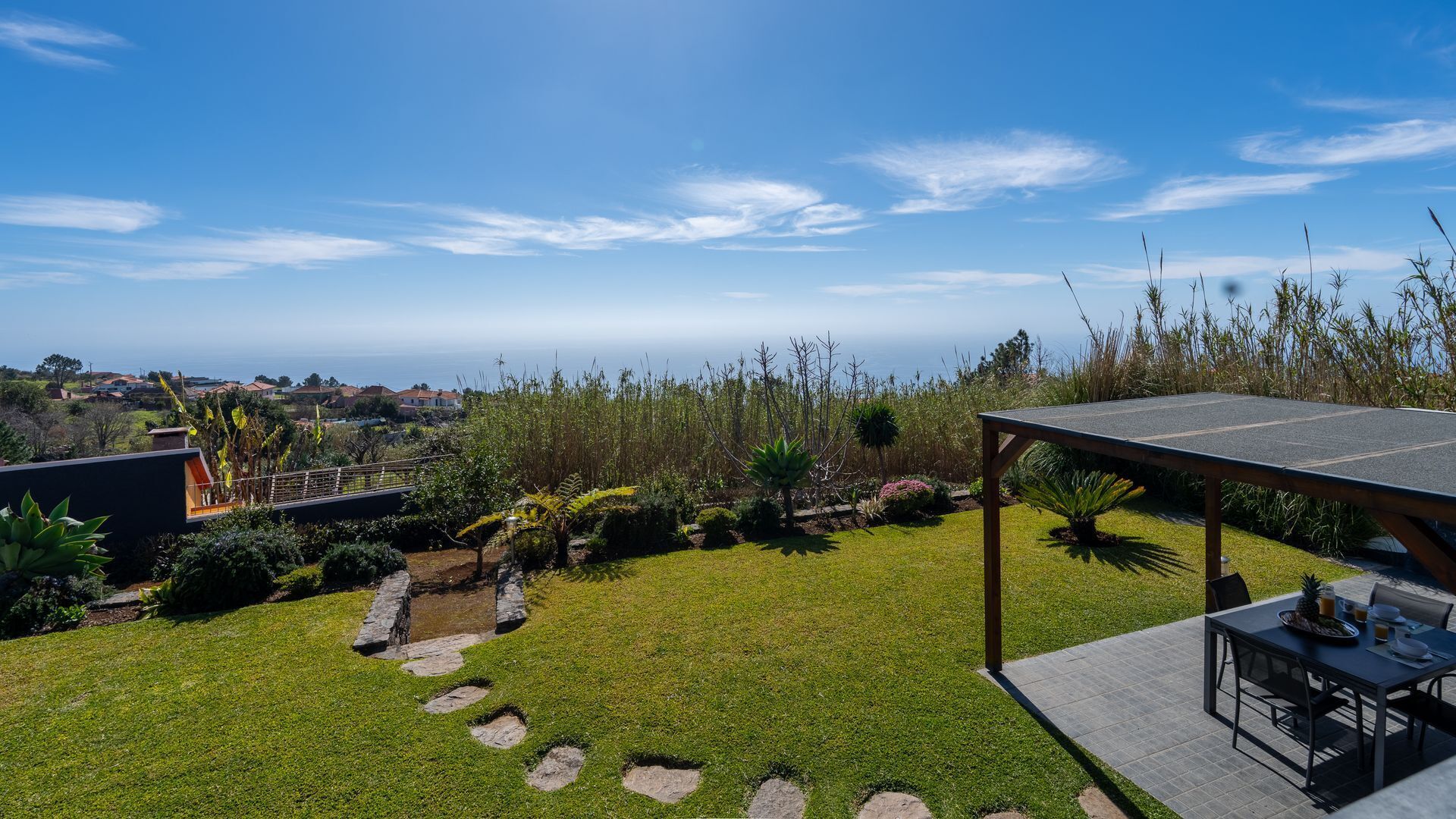 Ein Garten mit Terrasse, einem Steinweg und Blick auf das Meer.